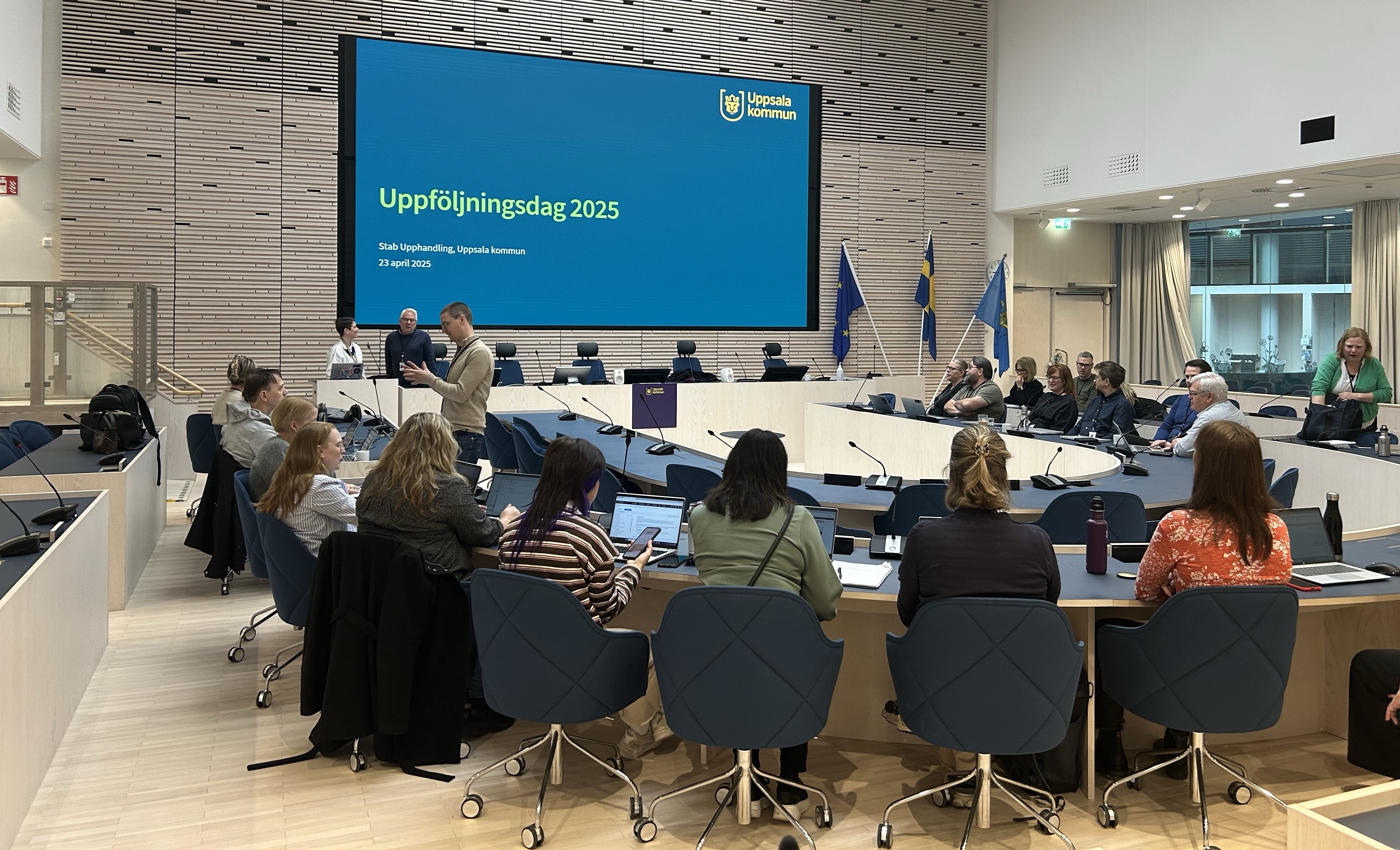 Cirka 30 personer runt ett U-format bord i ett konferensrum och tittar p&aring; en sk&auml;rm som det st&aring;r "Uppf&ouml;ljningsdag 2025" p&aring;. 