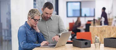 Två medarbetare i ett kontor samarbetar vid en laptop.