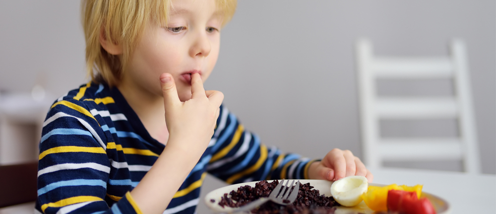 Ett förskolebarn i randig tröja äter hälsosam mat.