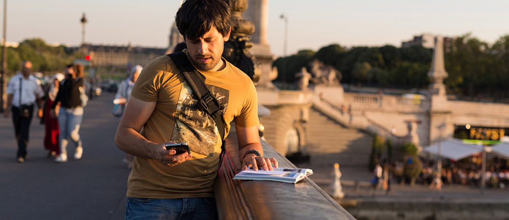 En ung man kollar sin telefon på en bro i Paris