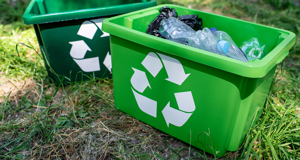 Gröna plastlådor  med återvinningssymbol, fyllda med plastflaskor