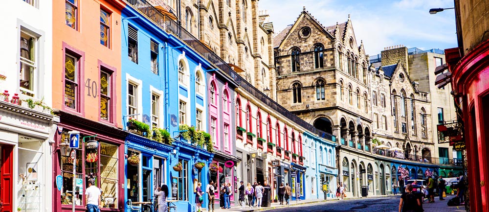Människor promenerar på en gata med gamla färgglada hus i Edinburgh.