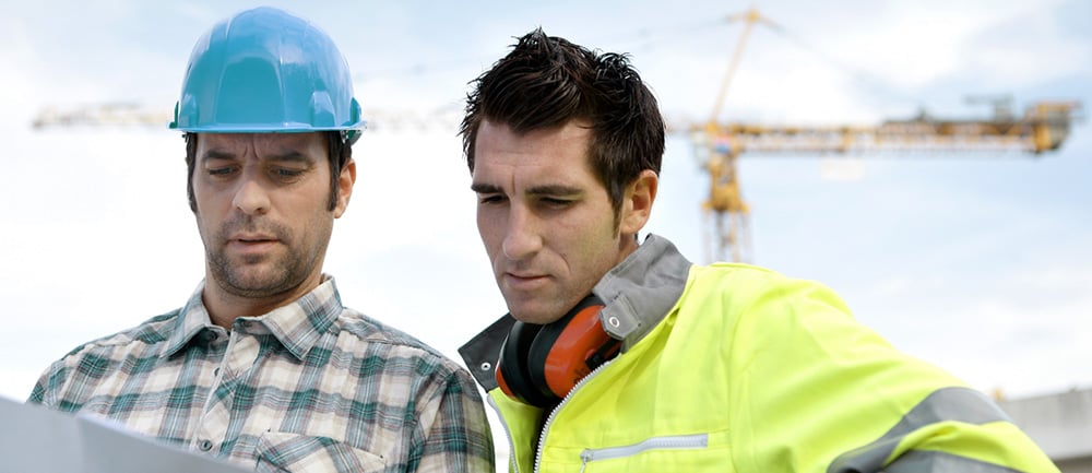 Två arbetare på en byggarbetsplats går igenom en ritning.