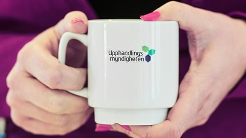 Händer håller mugg med Upphandlingsmyndighetens logotyp